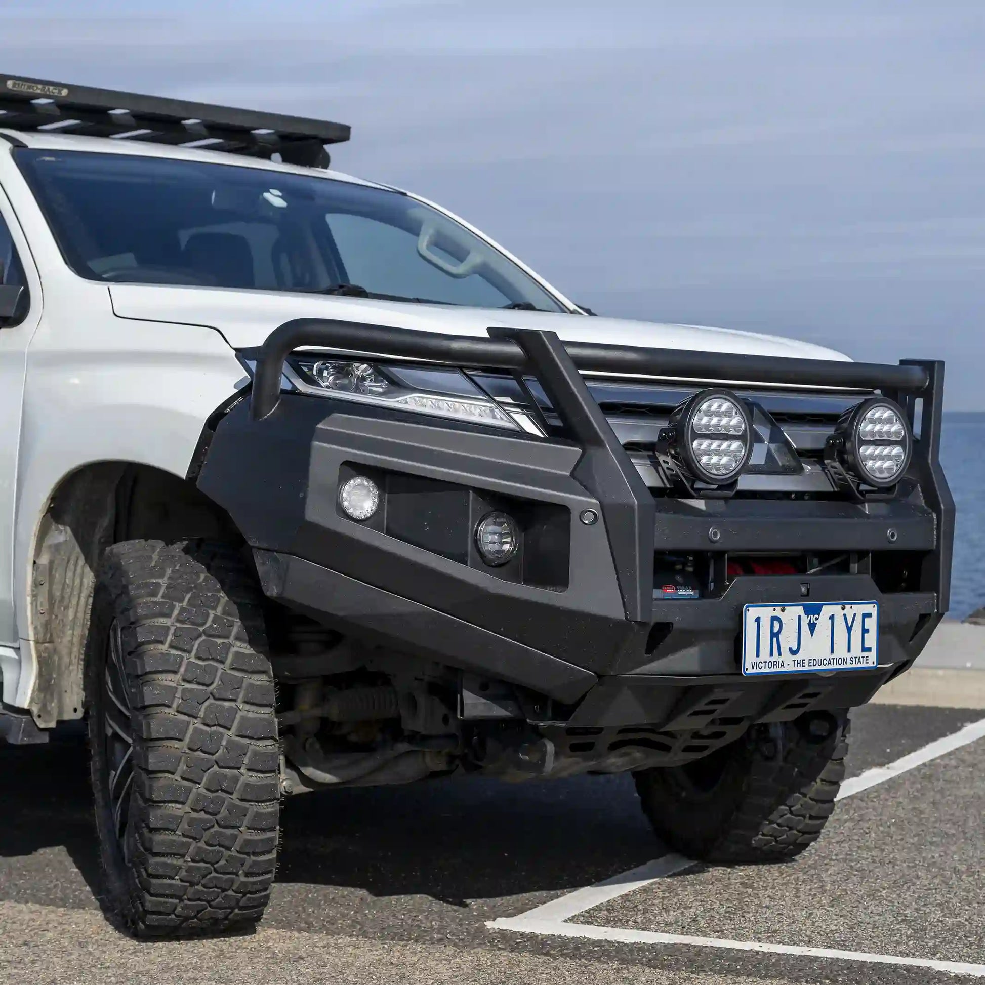 left side installed view of raxar loop type bull bar on mitsubishi pajero sport showing integrated fog lights airflow enhancing split pan design and full winch compatibility built for australian touring conditions and supplied nationwide by elevated 4x4