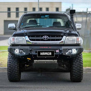 Front view of Toyota Hilux 1997–2005 with Hamer King Series Bull Bar, rugged matte black steel, ADR compliant with LED lights.