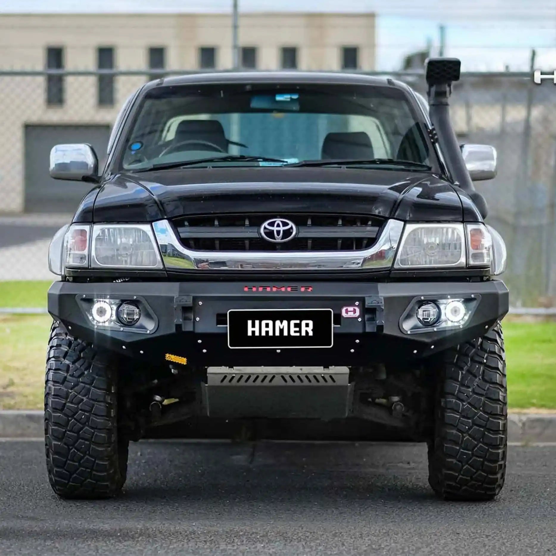 Front view of Toyota Hilux 1997–2005 with Hamer King Series Bull Bar, rugged matte black steel, ADR compliant with LED lights.