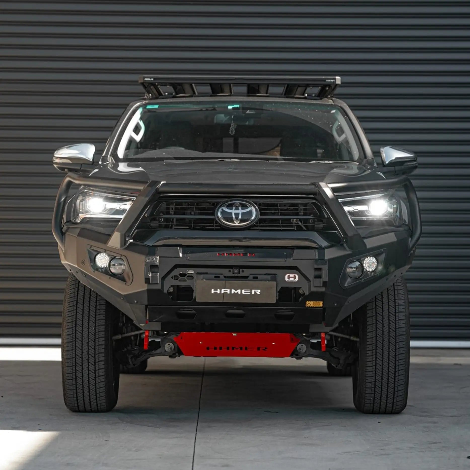 Angled front view of Toyota Hilux (2020 – 2023) showcasing Hamer King Series Plus Bull Bar with integrated parking sensors, light bar slot, recovery points, and rugged triple loop styling.